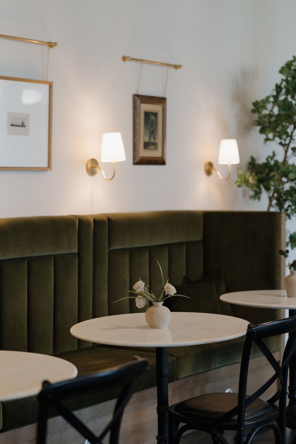 Green velvet banquette with marble bistro tables and brass sconces