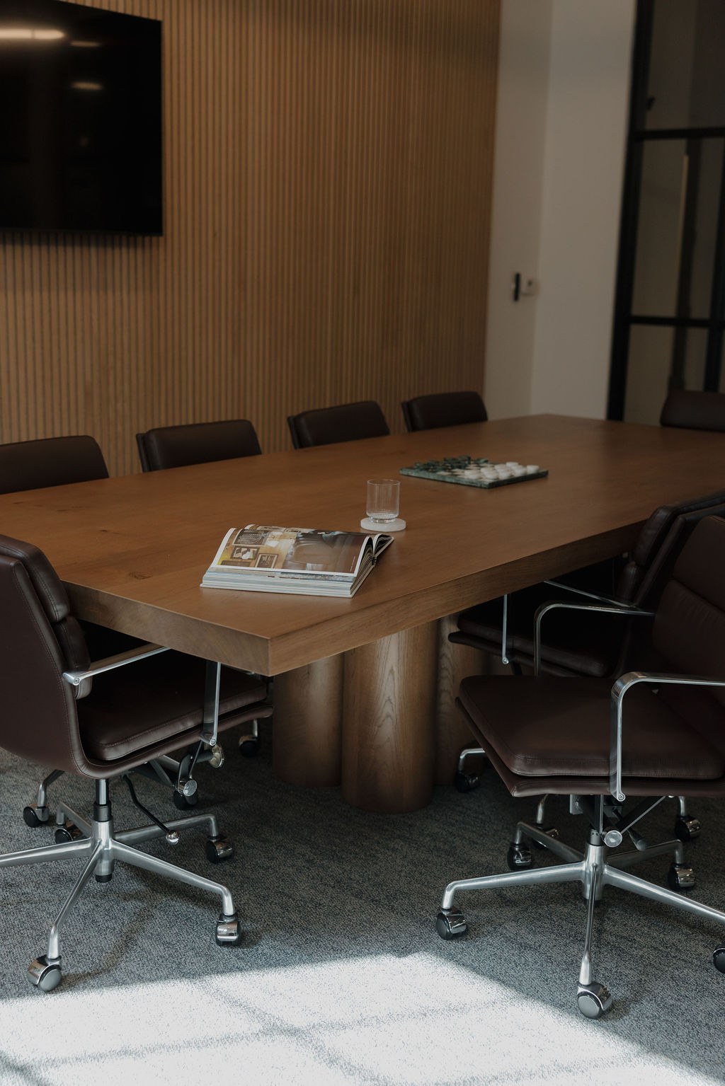 Conference room with a warm oak table, leather chairs and a slatted wood wall
