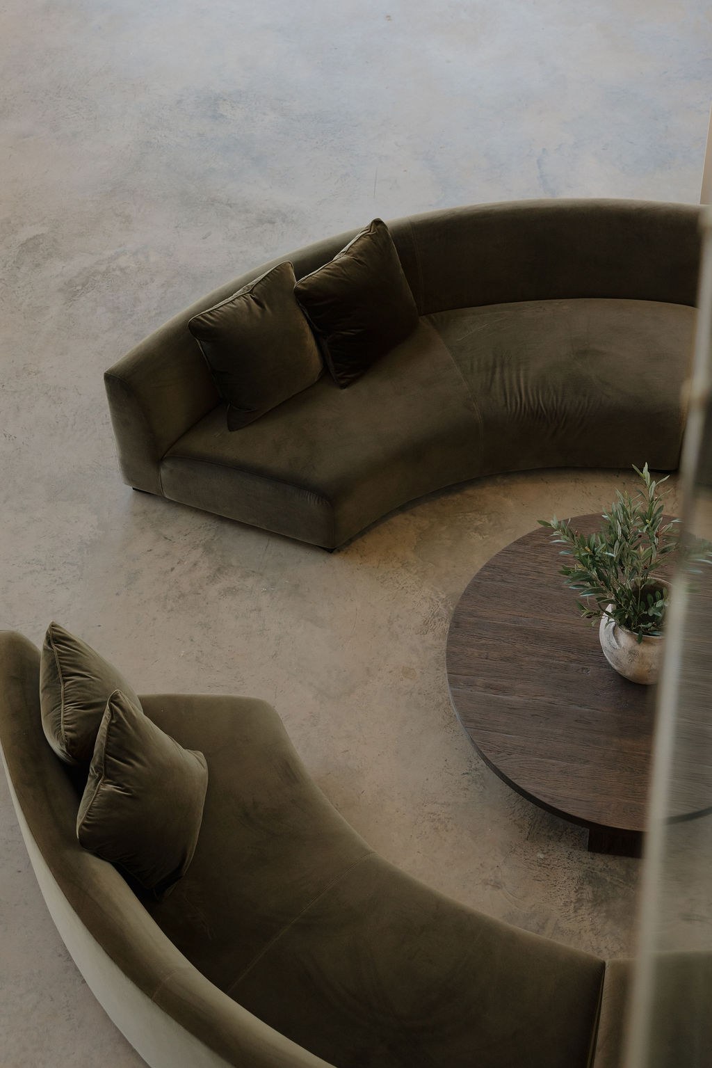 Two curved olive velvet sofas around a round wood coffee table, seen from above