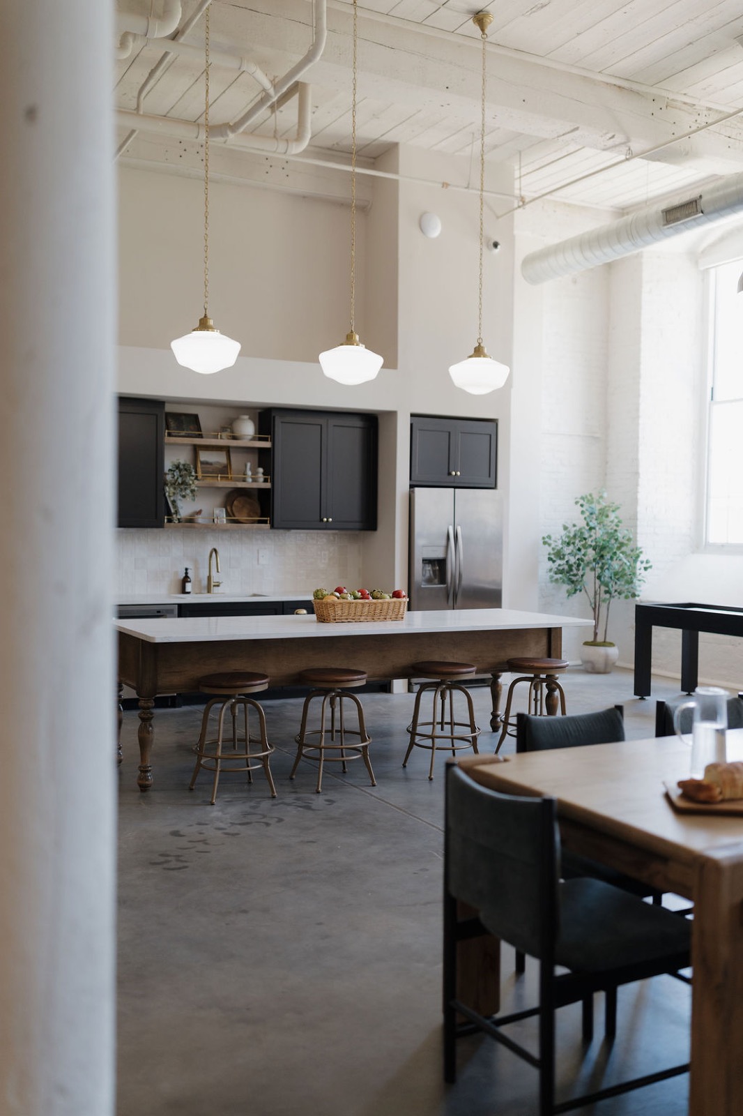Open kitchen with a long island, brass-trimmed pendant lights, and counter stools between white columns