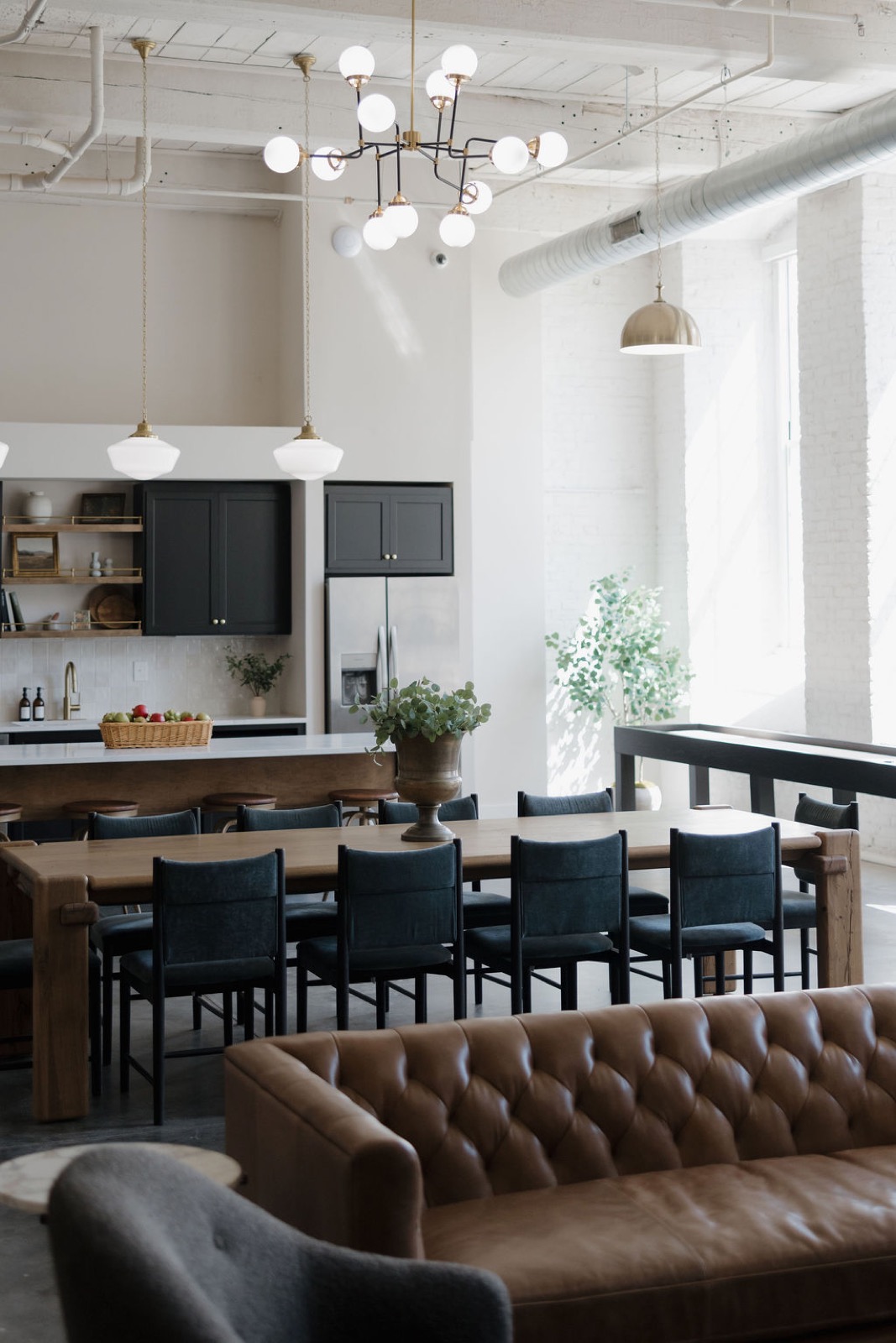 An open-plan room with a kitchen island, a long dining table with blue chairs, and a tufted leather sofa