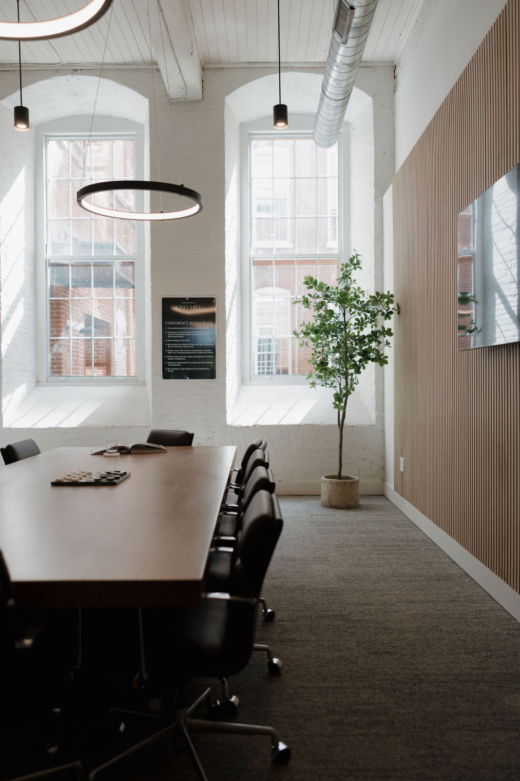 The conference room with arched windows, a ring pendant, a tall plant, and a long wood table