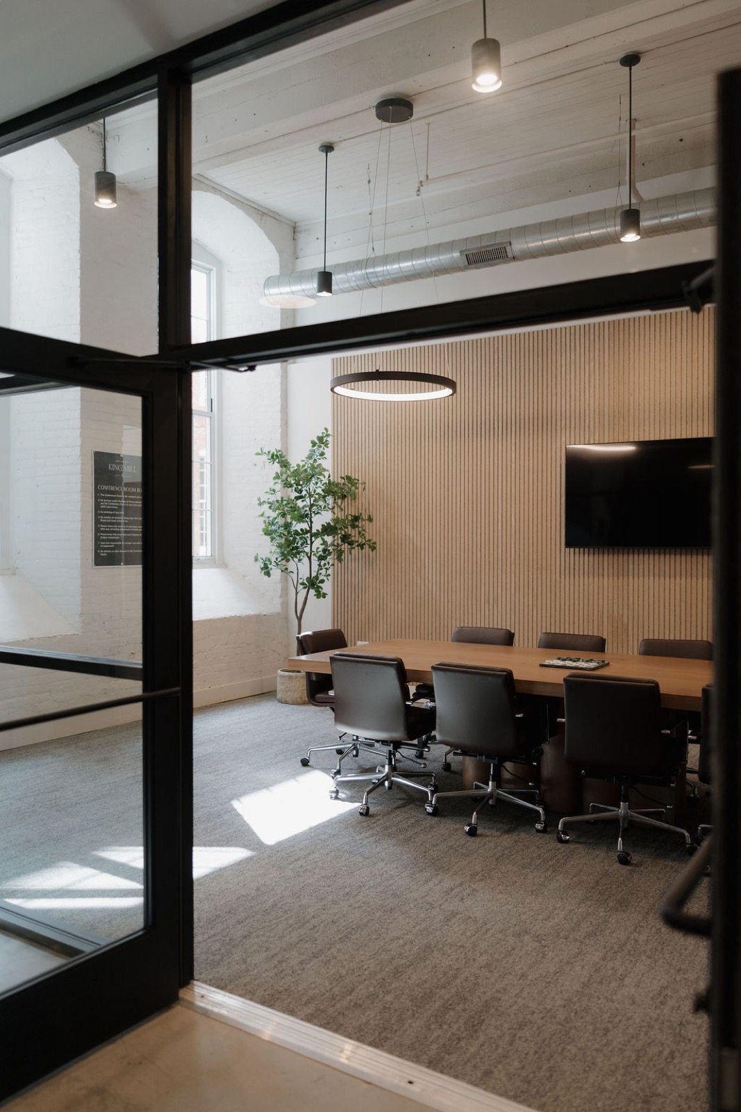 The glass-walled conference room seen through a black steel door, with a ring pendant and a wood slat wall