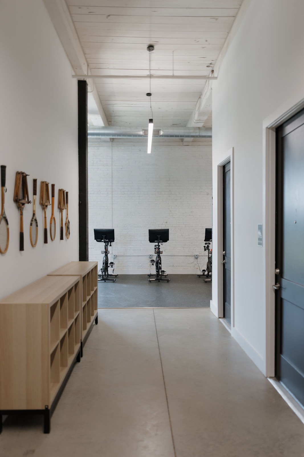 A hallway with vintage tennis rackets on the wall and wood cubbies, leading to a cycling studio