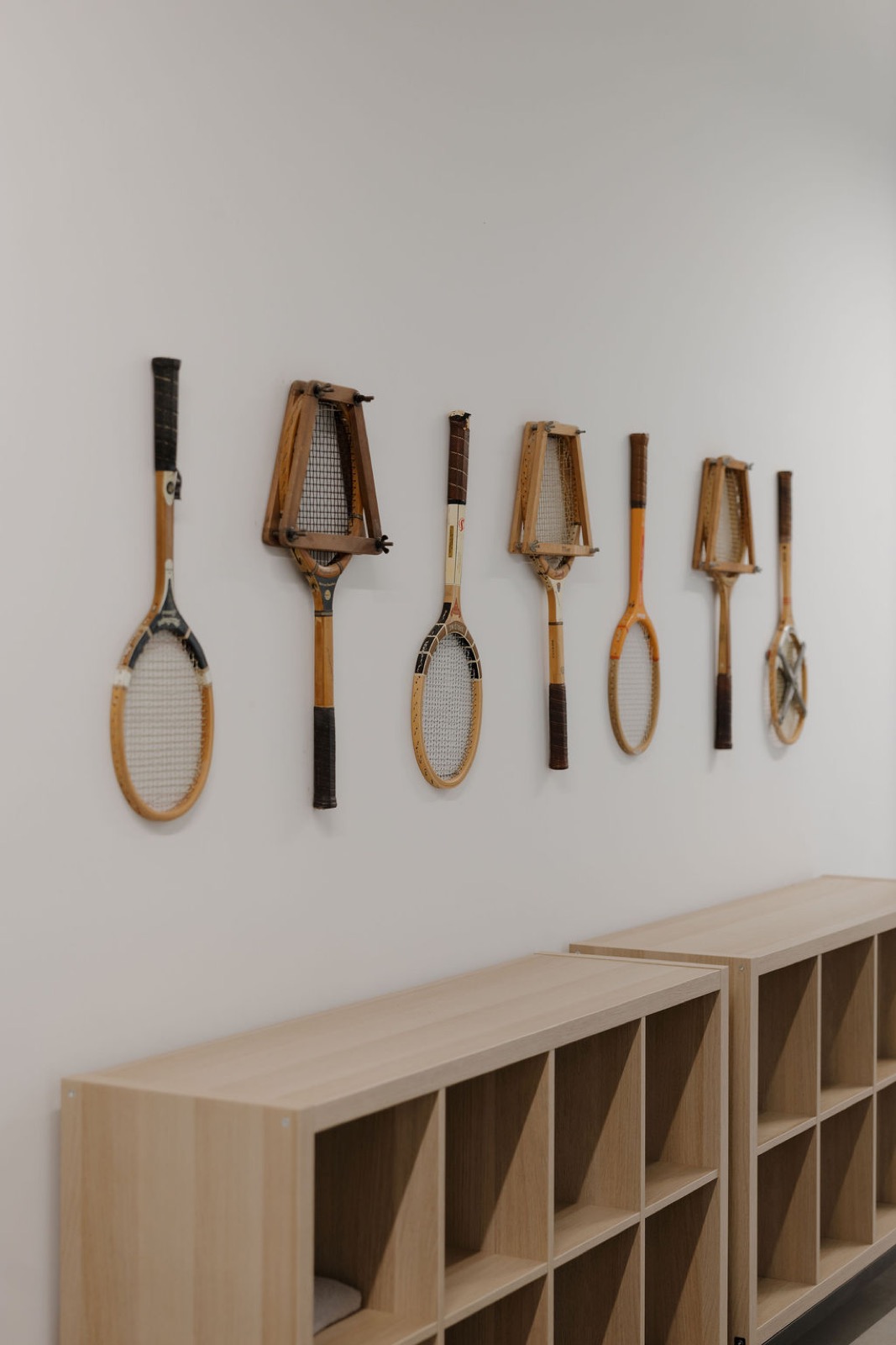 Seven vintage wooden tennis rackets mounted on a white wall above wood cubbies