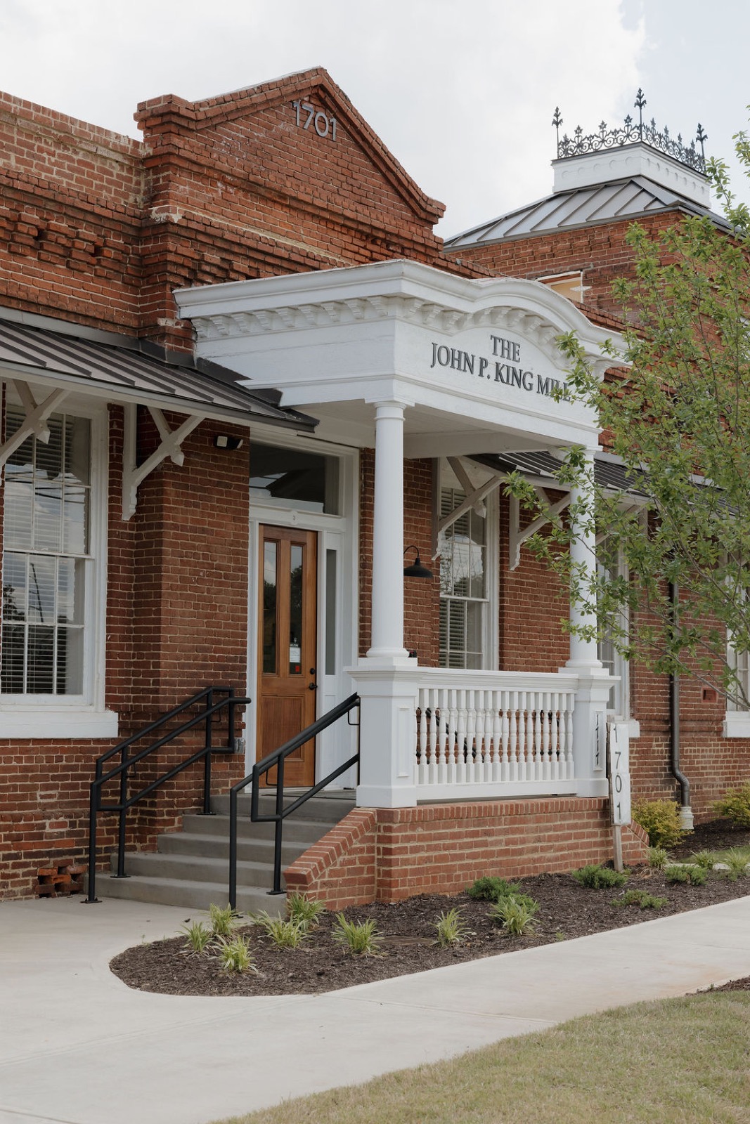 The brick entrance of the John P. King Mill leasing office with a white portico and wood door