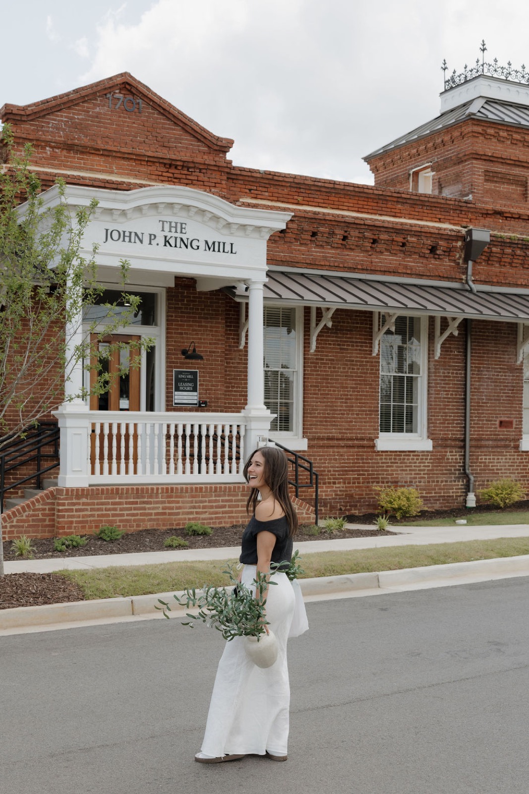 A woman carrying olive branches in a vase across the street in front of the leasing office entrance