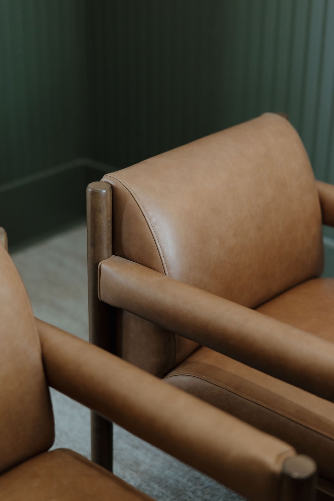 Close view of tan leather armchairs with wood frames against green paneling