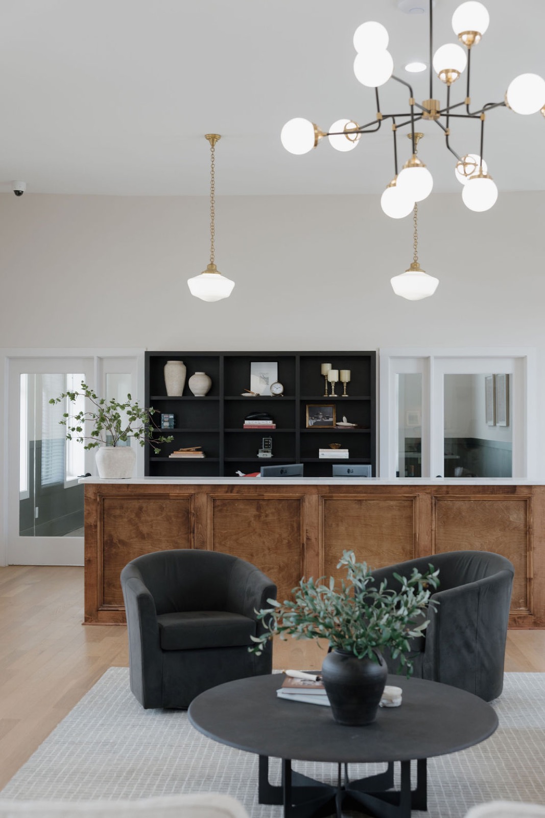 The leasing lobby with two black swivel chairs, a round table, and a globe chandelier in front of the reception desk