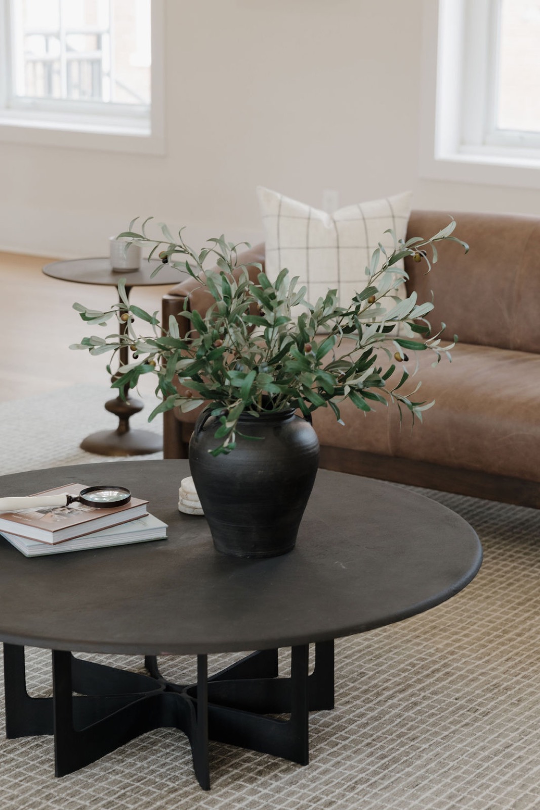 A black round coffee table with an olive-branch vase in front of a tan leather sofa