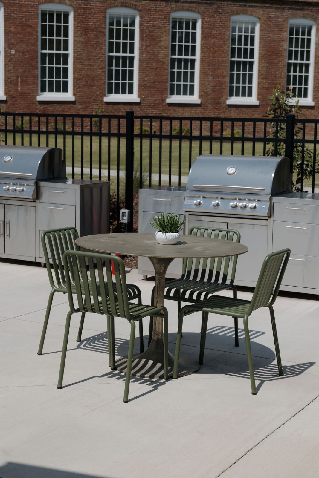 An outdoor kitchen with two stainless grills and a bistro table with olive chairs
