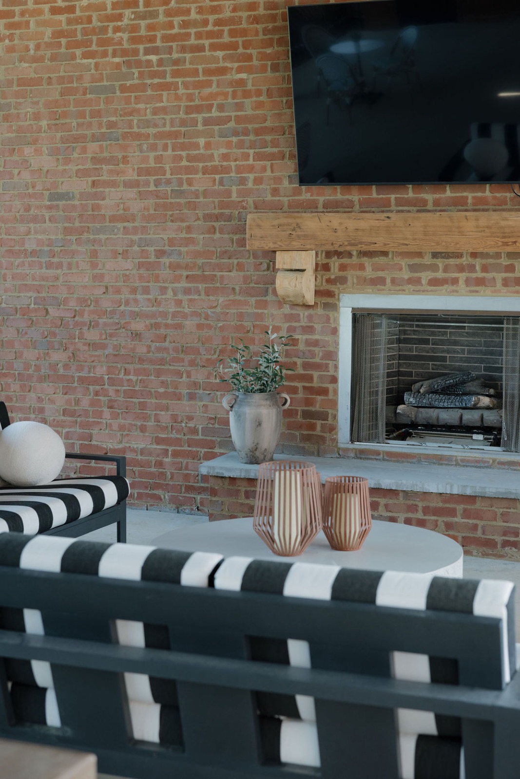 A covered lounge with black-and-white striped sofas in front of a brick fireplace and television