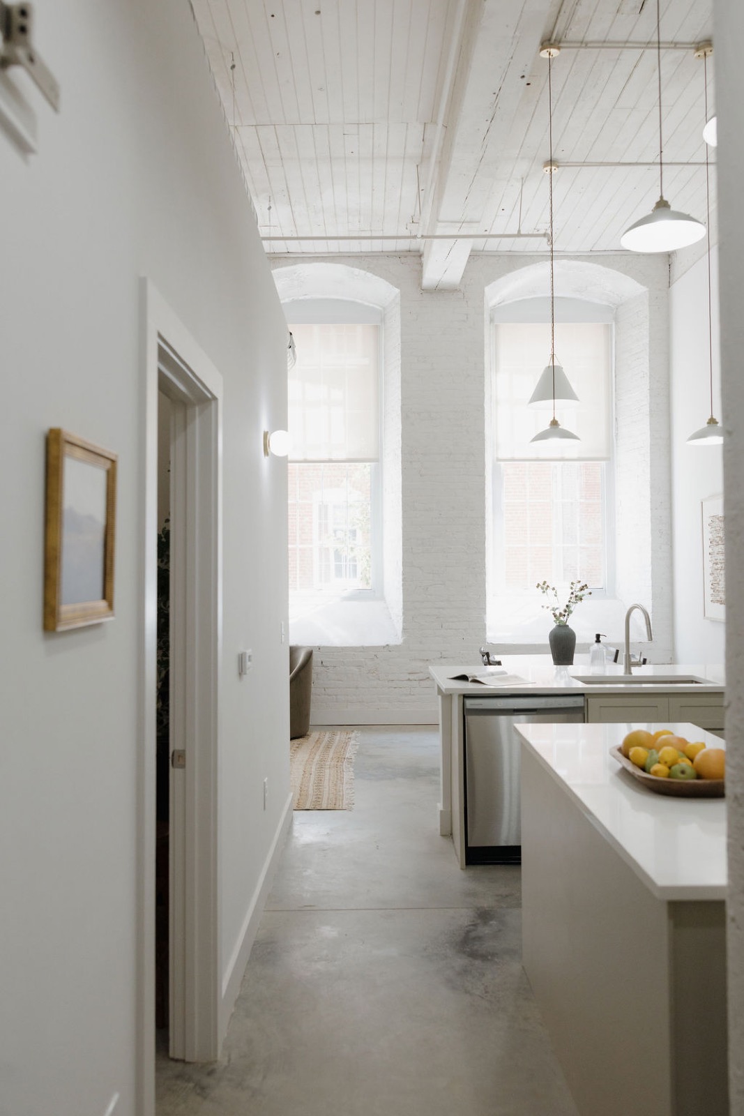 A hallway view toward the kitchen island and two arched windows beneath a whitewashed wood ceiling