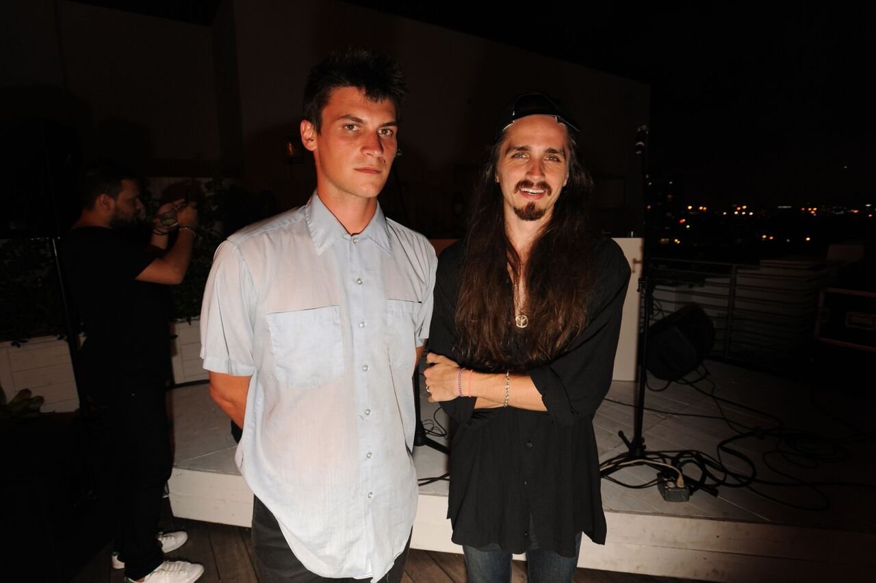 Two men standing in front of a rooftop stage with a microphone stand and cables