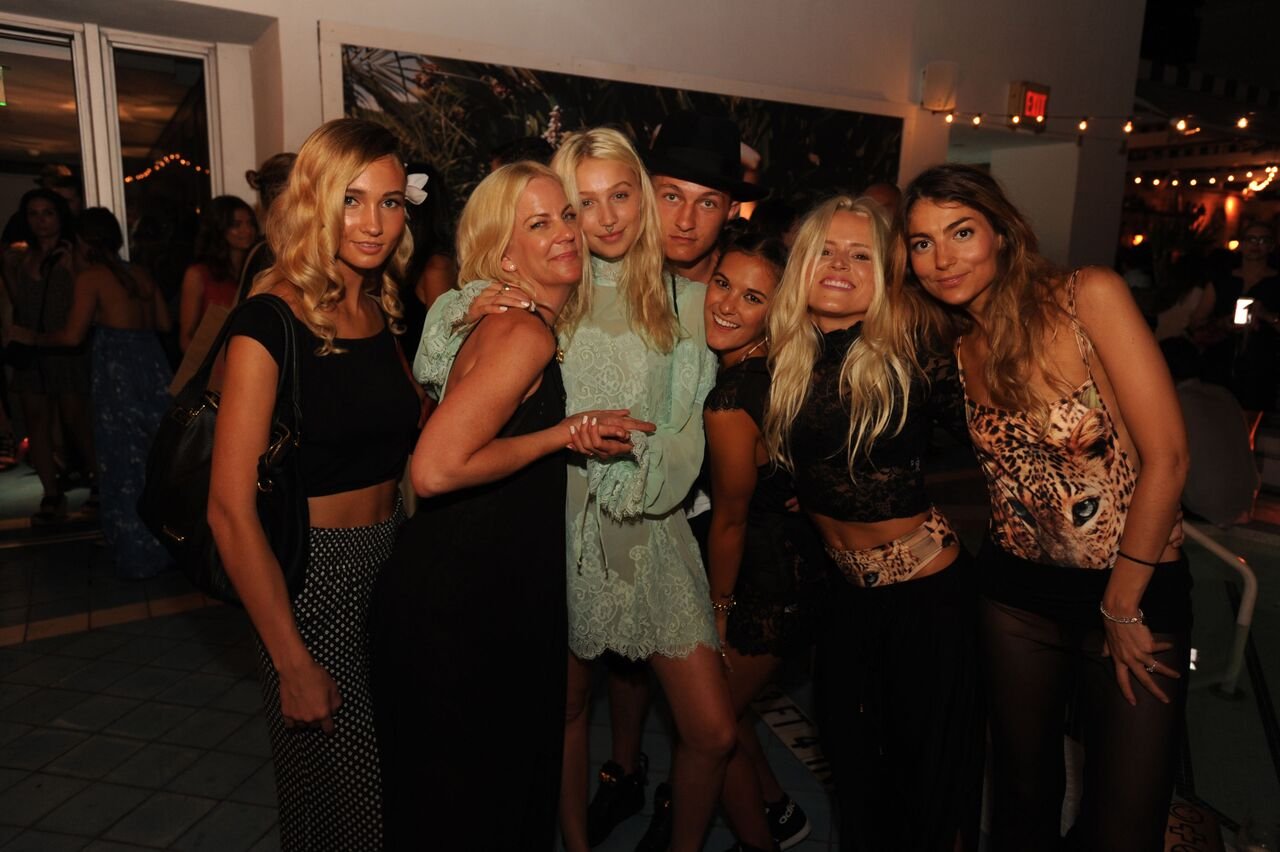 A group of friends embracing in front of a tropical-print mural at the party