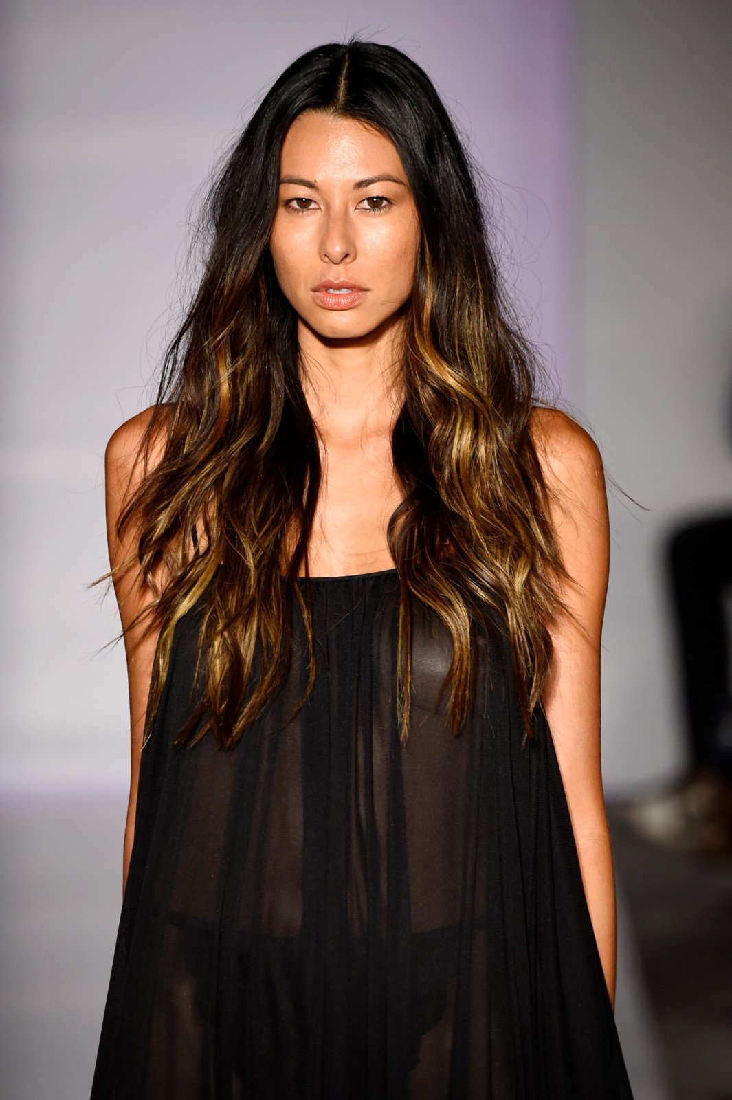A model with long dark hair in a sheer black swing dress