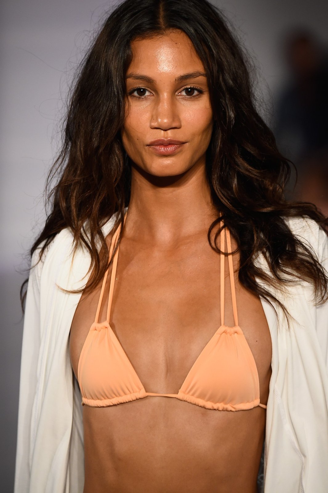 A close portrait of a model in a peach triangle bikini top and a white open jacket