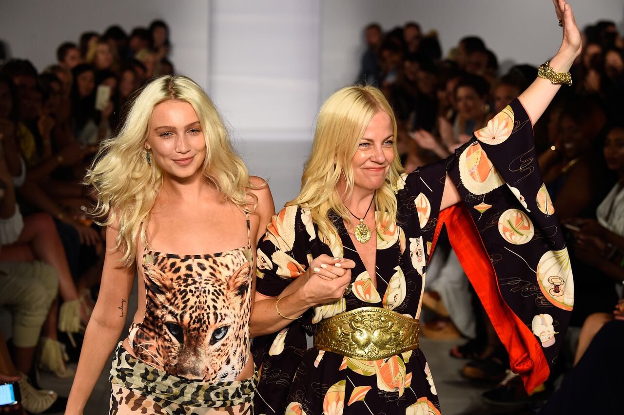 A designer in a black printed kimono and gold belt waving to the audience beside a model in a leopard-face bodysuit