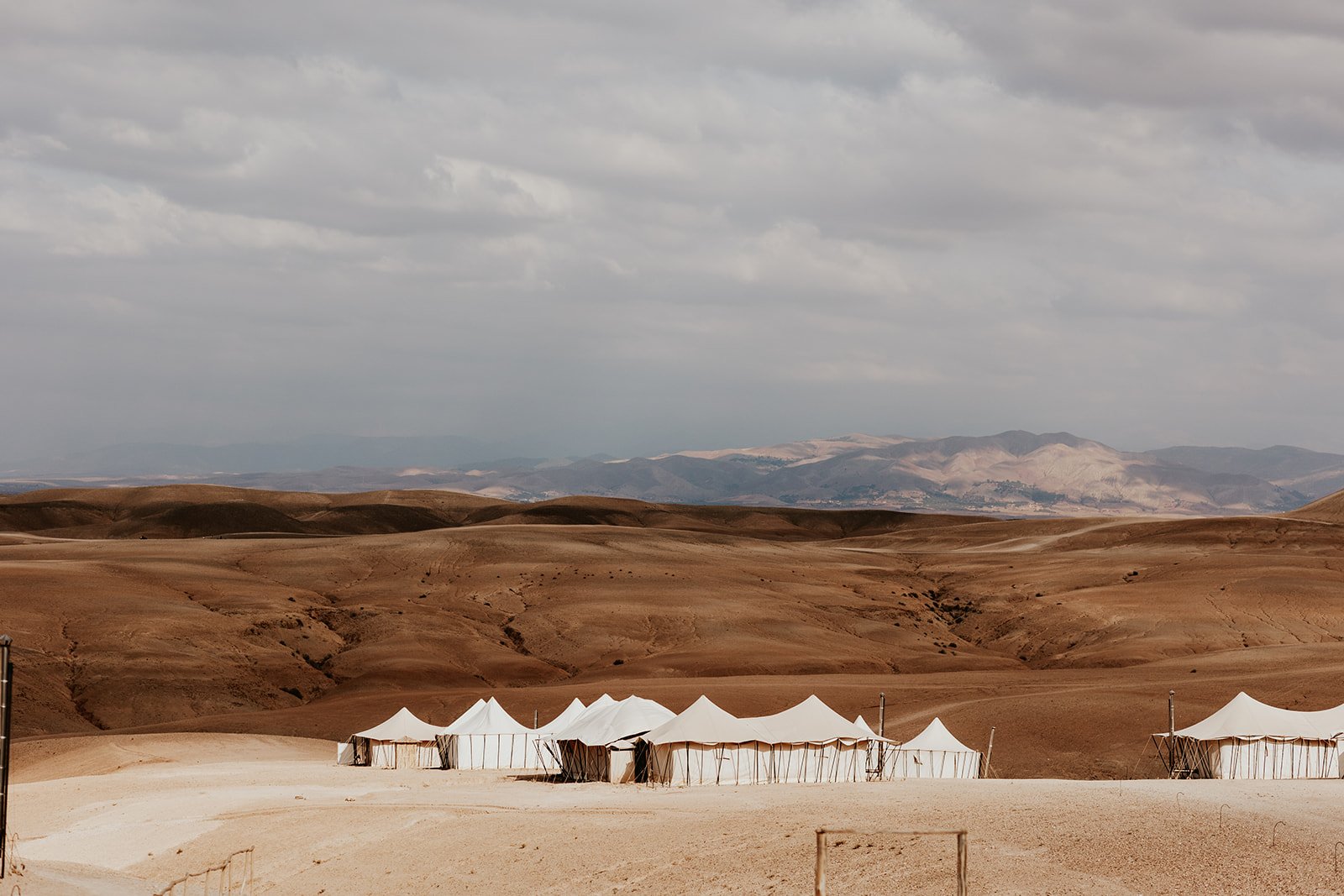 White canvas tents on a hillside in the Agafay Desert beneath a cloudy sky