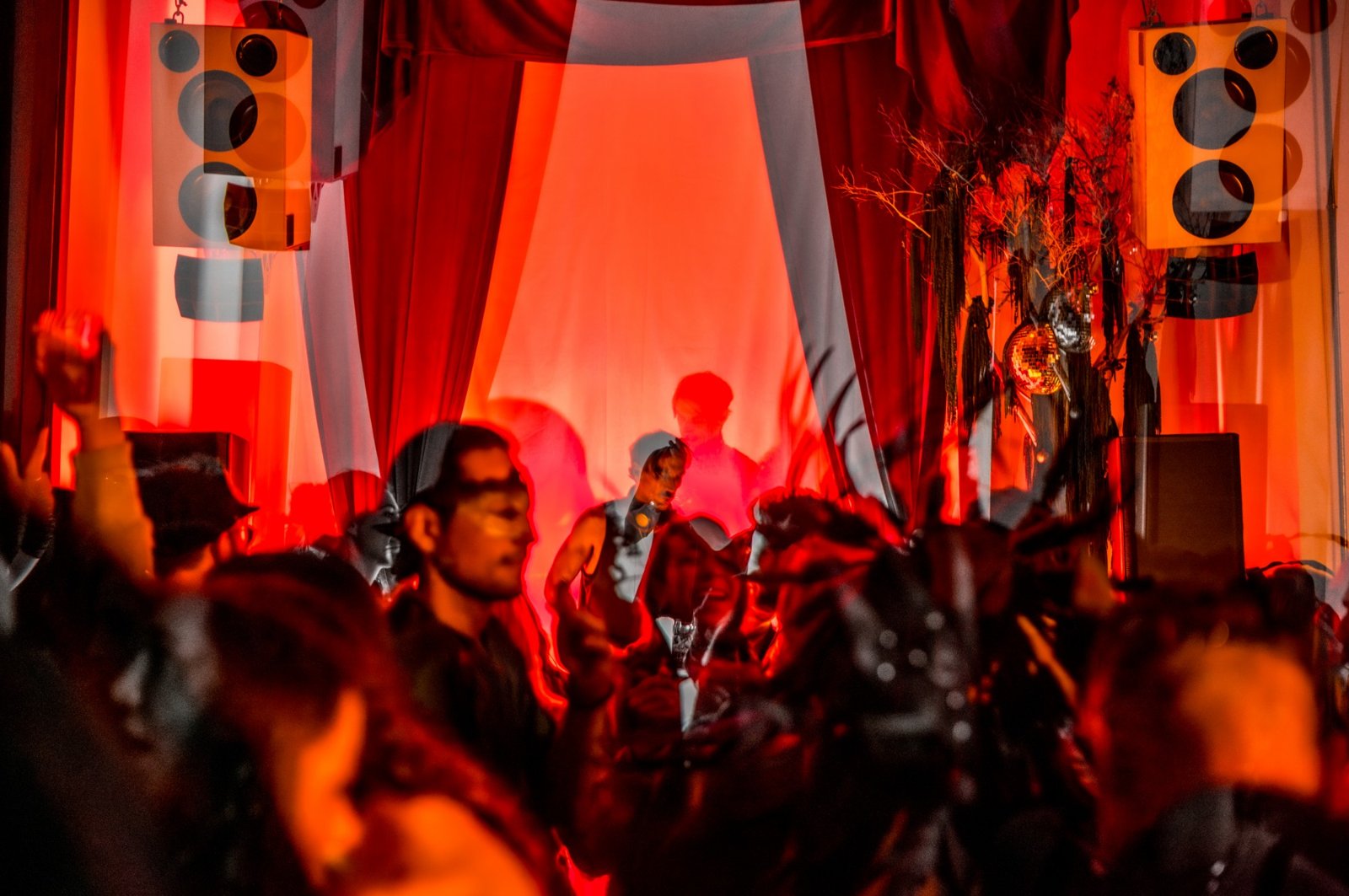 Guests in masks dancing in front of a DJ stage hung with red velvet curtains, speakers, and a disco ball