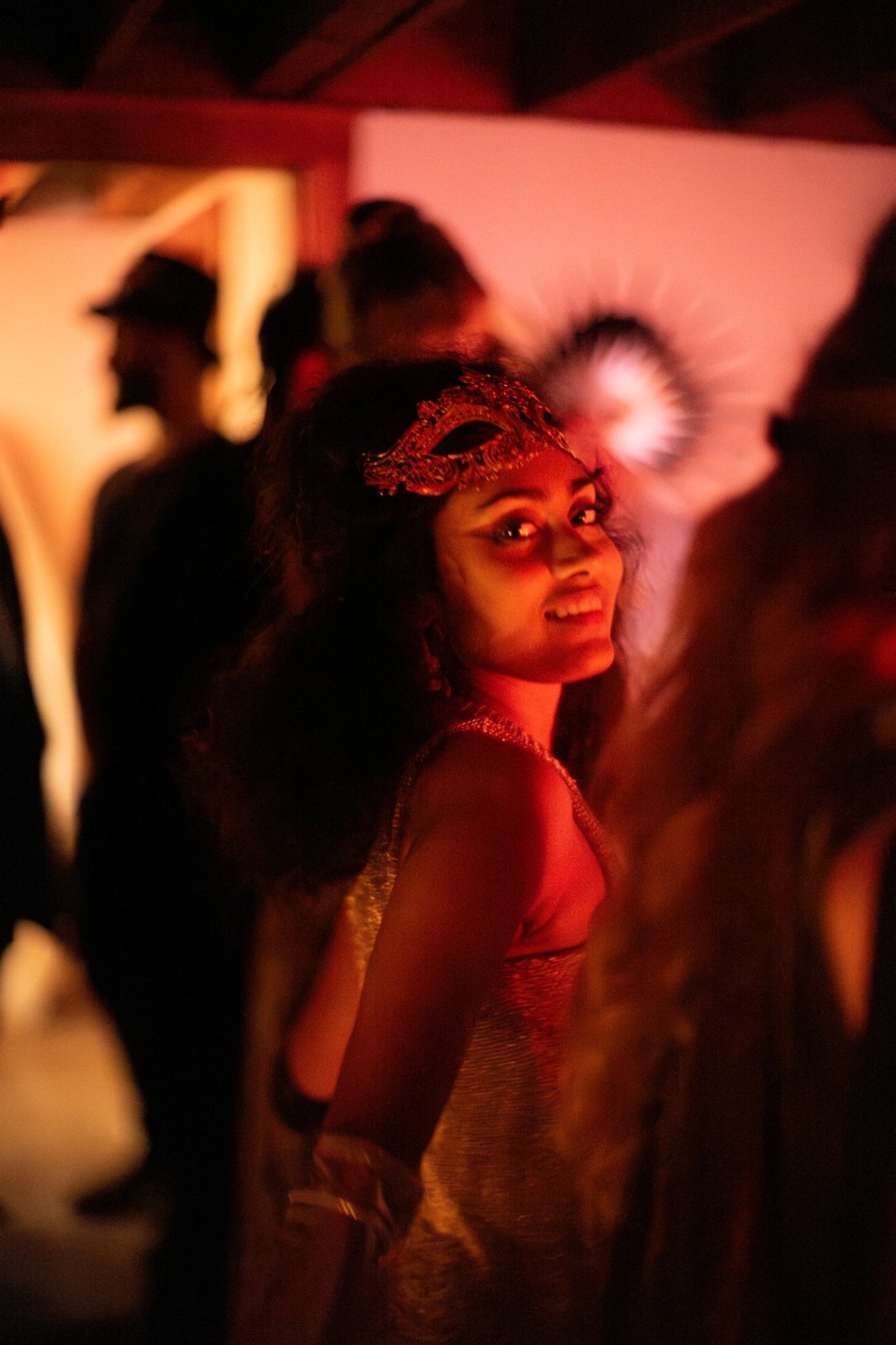 A guest in a lace mask looking over her shoulder in red light