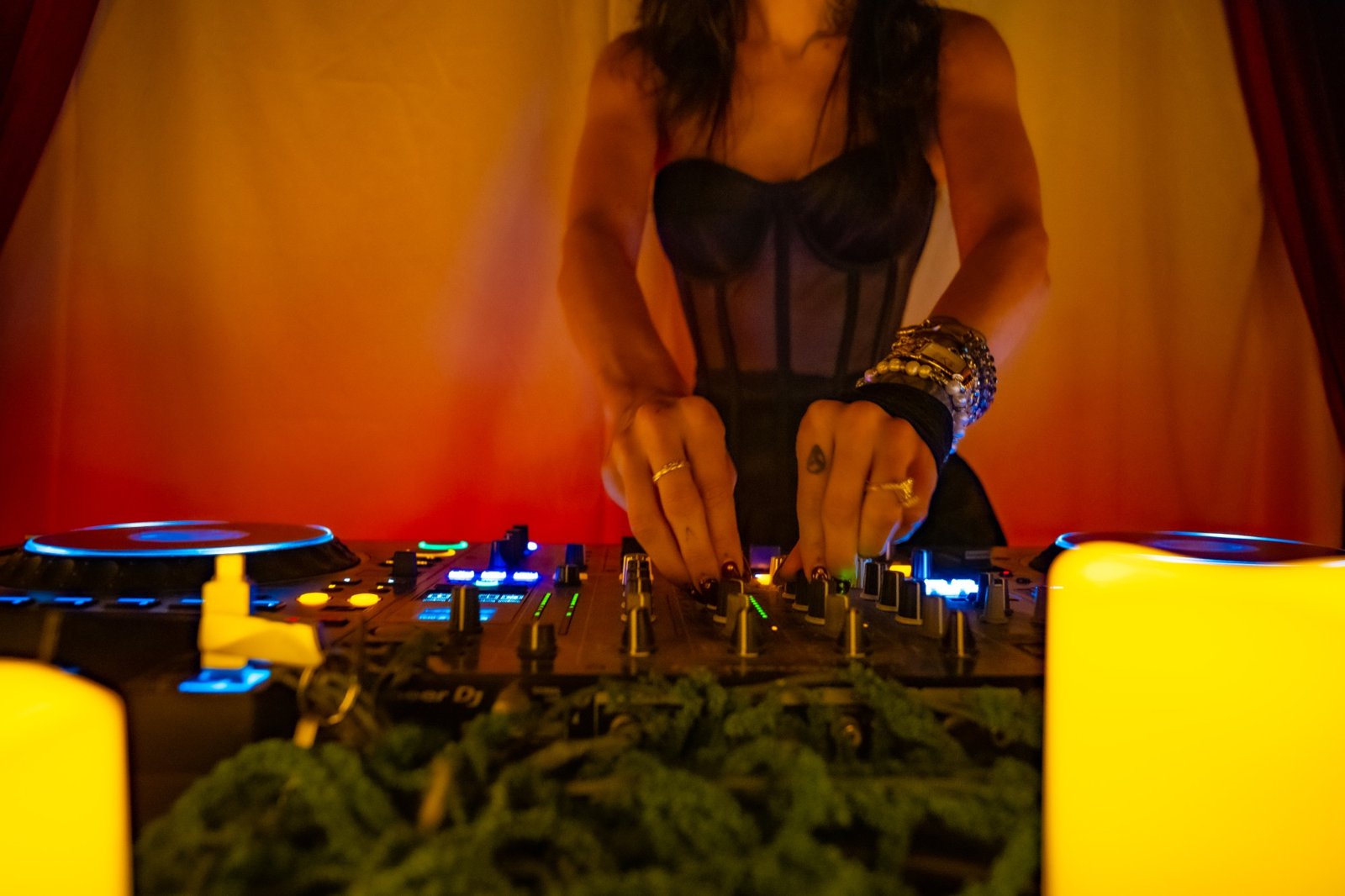 A DJ mixing at turntables with candles and green garland in front of a glowing curtain