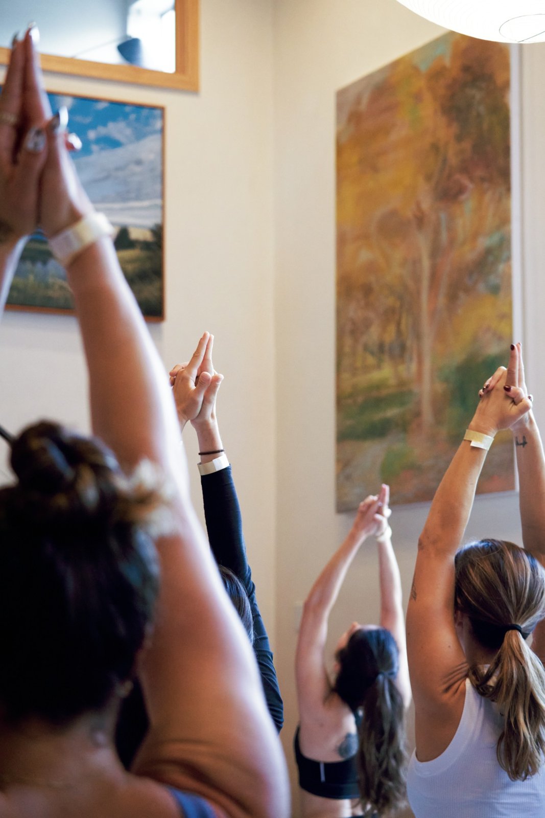 Yoga students raising joined hands overhead beneath a large landscape painting