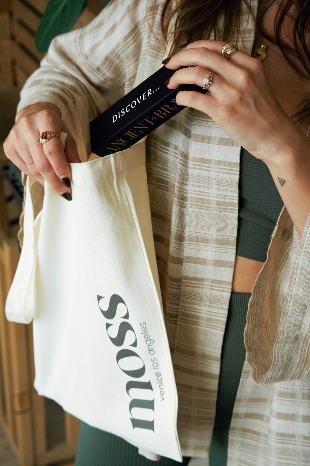 A woman pulling a card box from a Moss Venice Los Angeles tote bag
