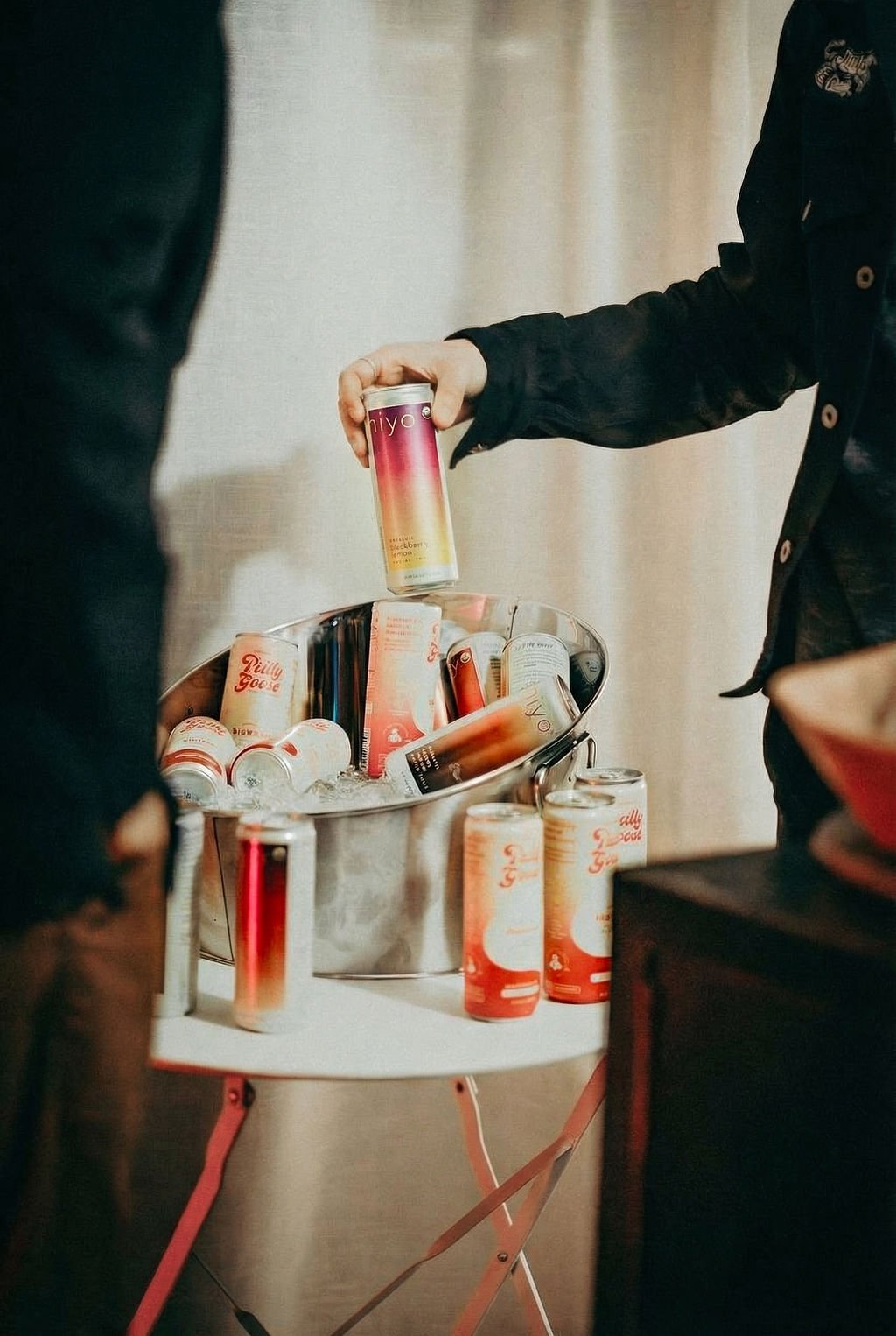 A hand placing a can on a bucket of iced sponsor beverages on a small table