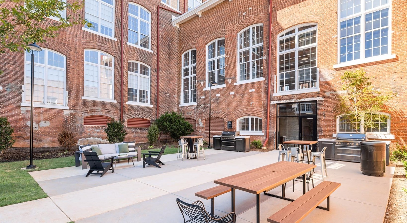 A brick courtyard with a lounge of sofa and Adirondack chairs, bar tables, grills, and a picnic table