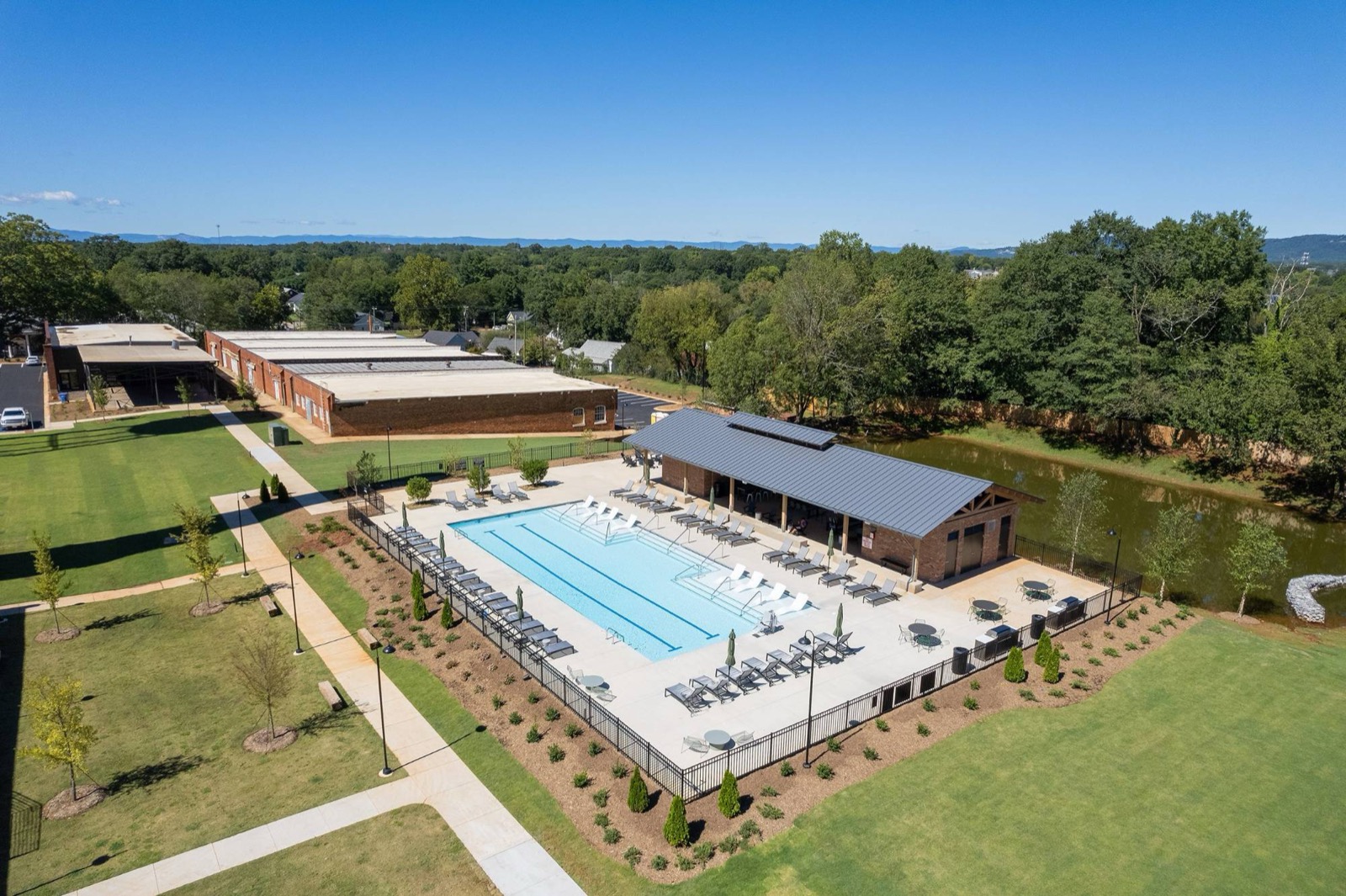 An aerial view of the pool and covered pavilion beside a pond, with lawns and the mill buildings around them