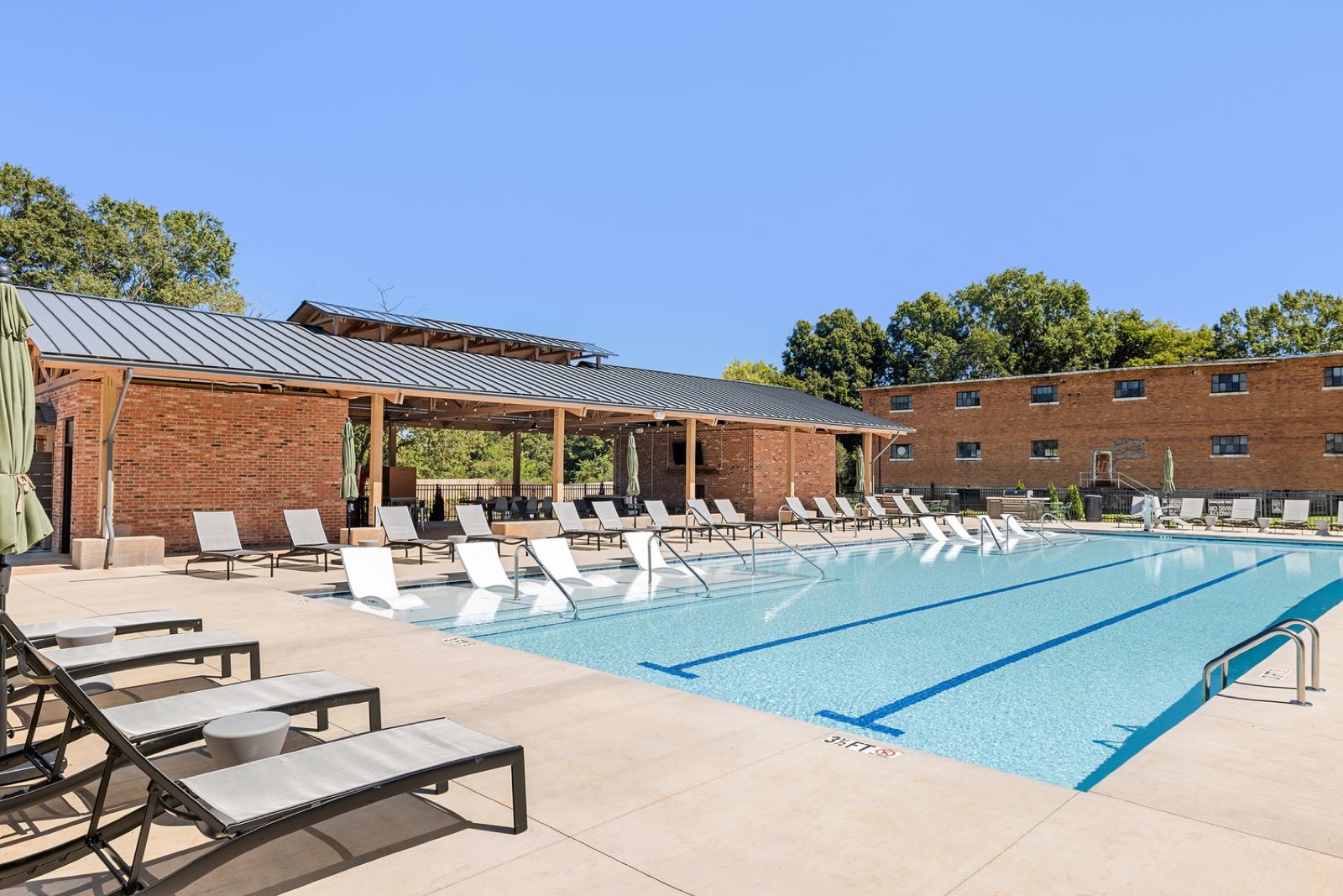 The pool with white in-water loungers and the brick and metal-roof pavilion beside it