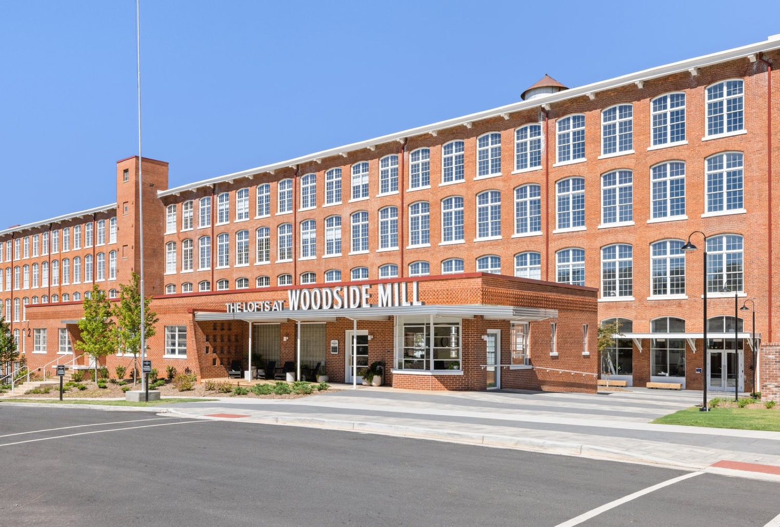 The mill entrance beneath a sign reading The Lofts at Woodside Mill, with the five-story brick building behind