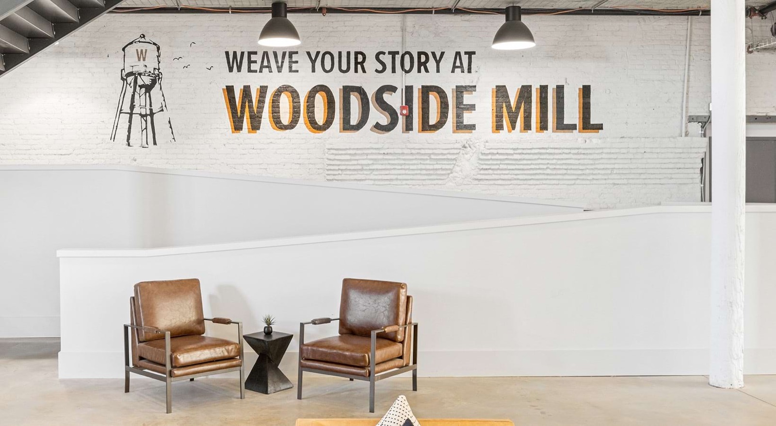 Two brown leather chairs in front of a painted brick wall mural reading Weave Your Story at Woodside Mill